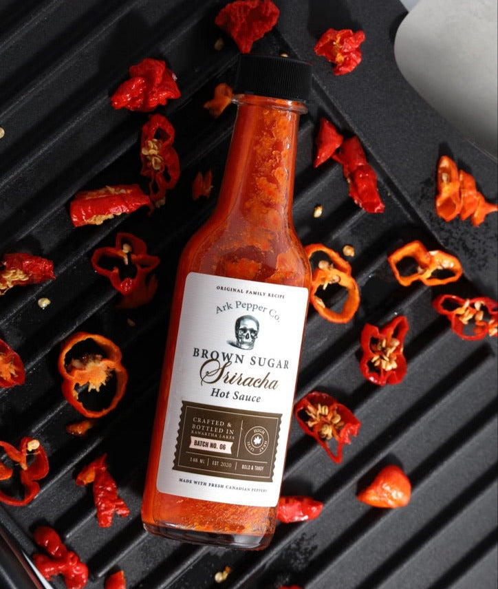 Ark Pepper Co. Brown Sugar Sriracha Hot Sauce on a grill with peppers