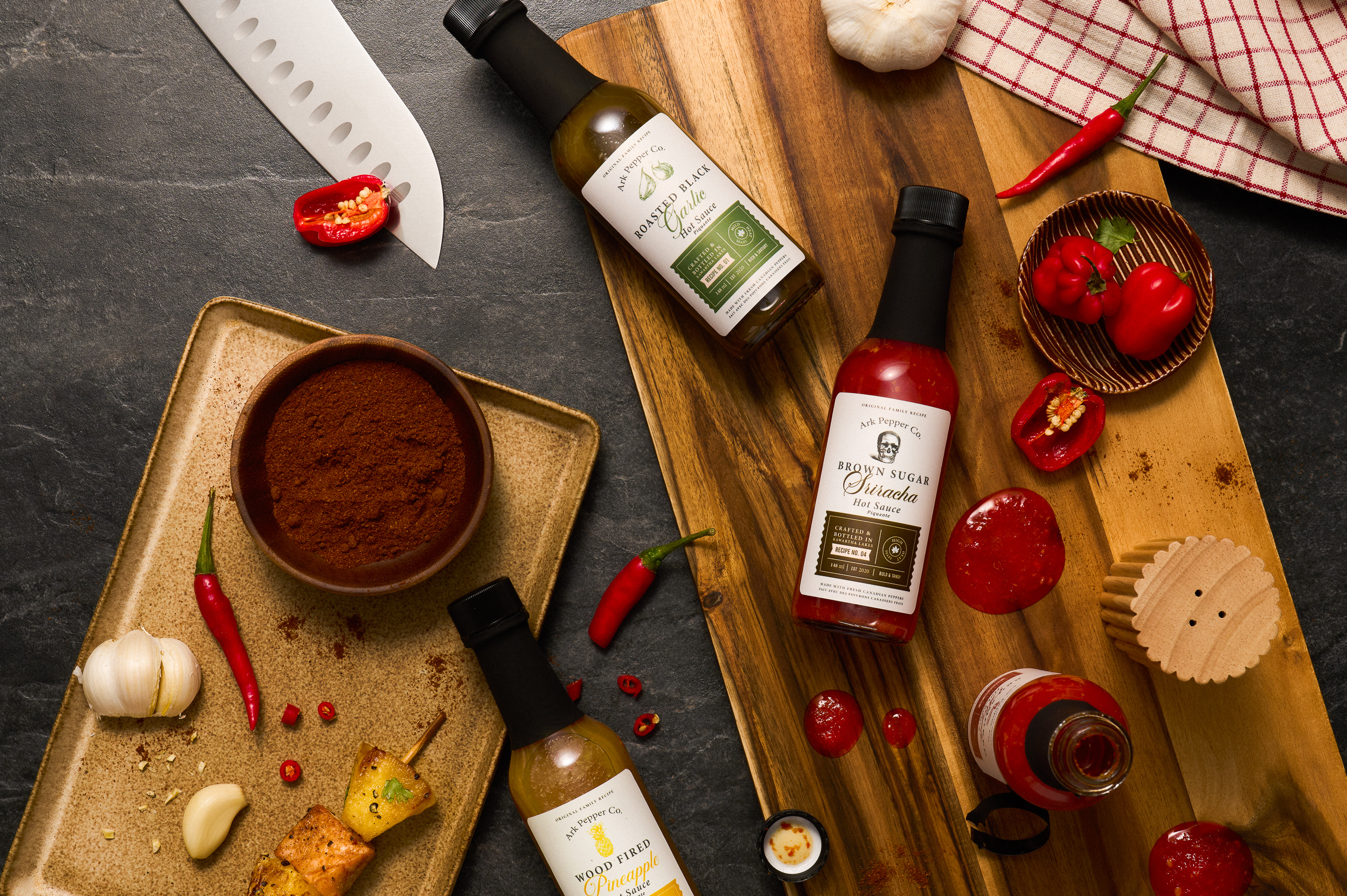Ark Pepper Co. hot sauce bottles on cutting board with chopped vegetables.